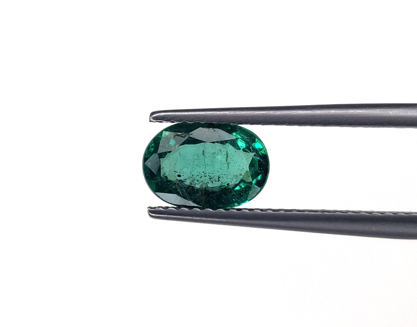 Emerald gemstone held by tweezers on a white background