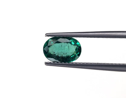 Emerald gemstone held by tweezers on a white background